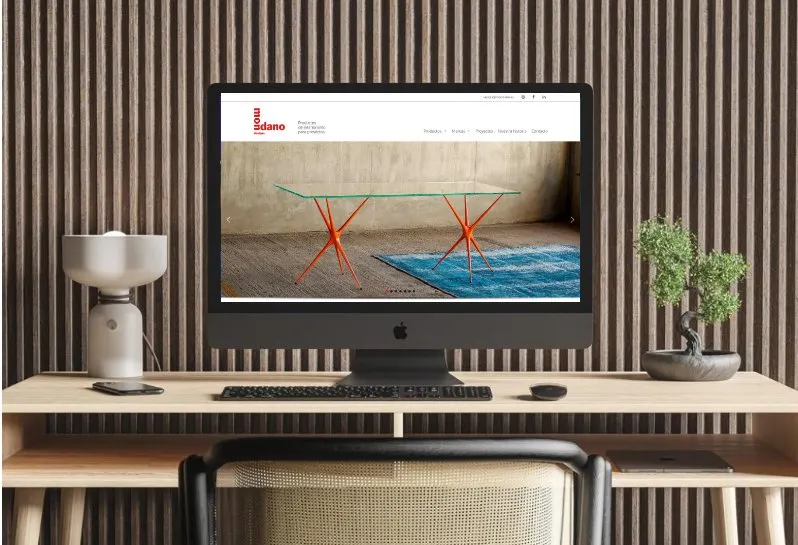 Web de Mondano en un monitor, con una mesa de diseño en la portada